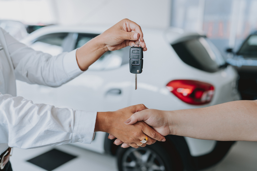 Car dealer handing car keys to their customer while shaking hands.
