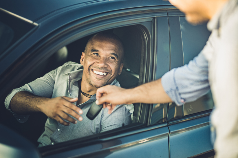 man handing car keys to a customer sitting in the front seat.