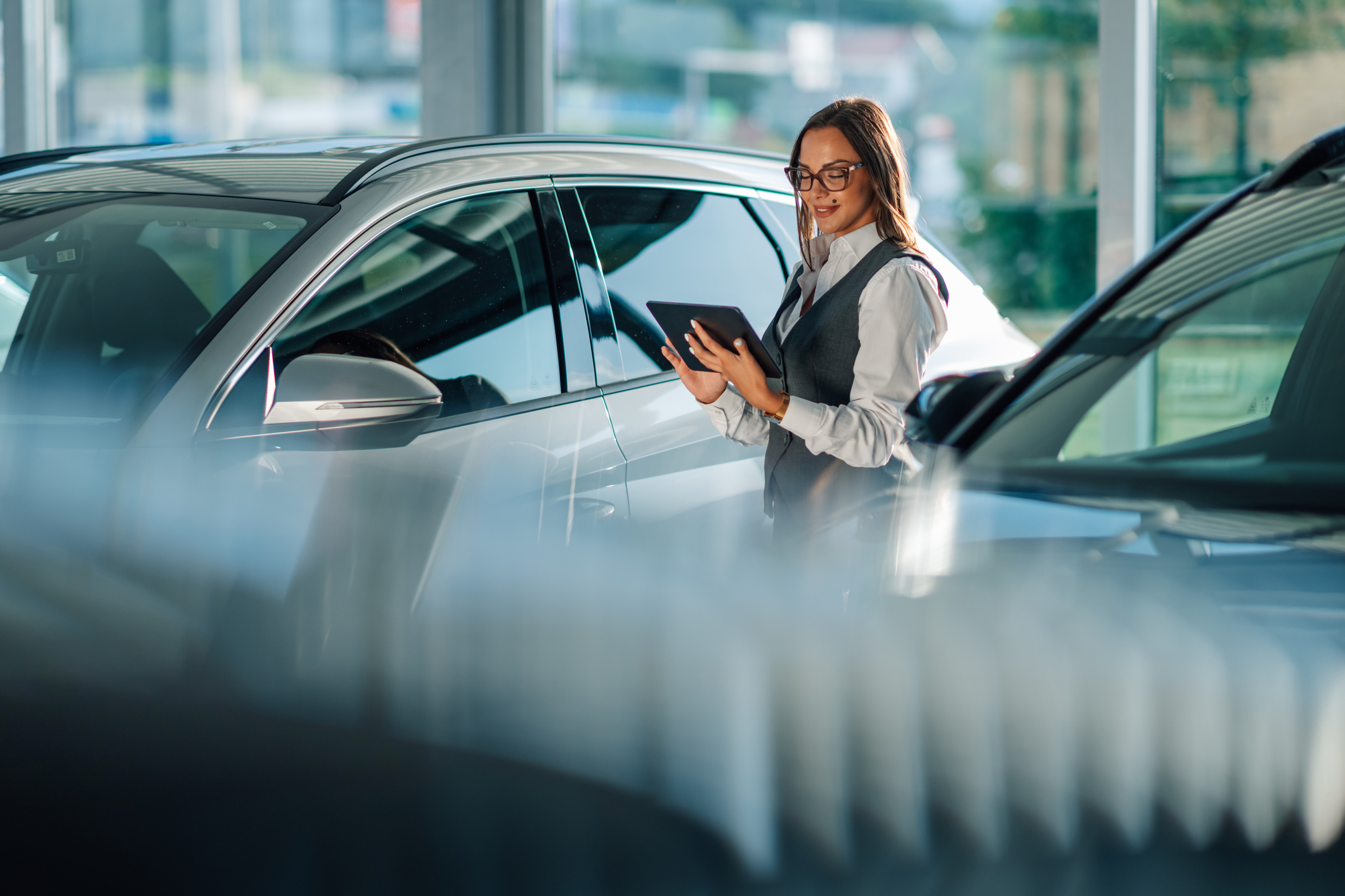 A professional woman is seen utilizing a tablet to assess cars in a modern dealership showroom.