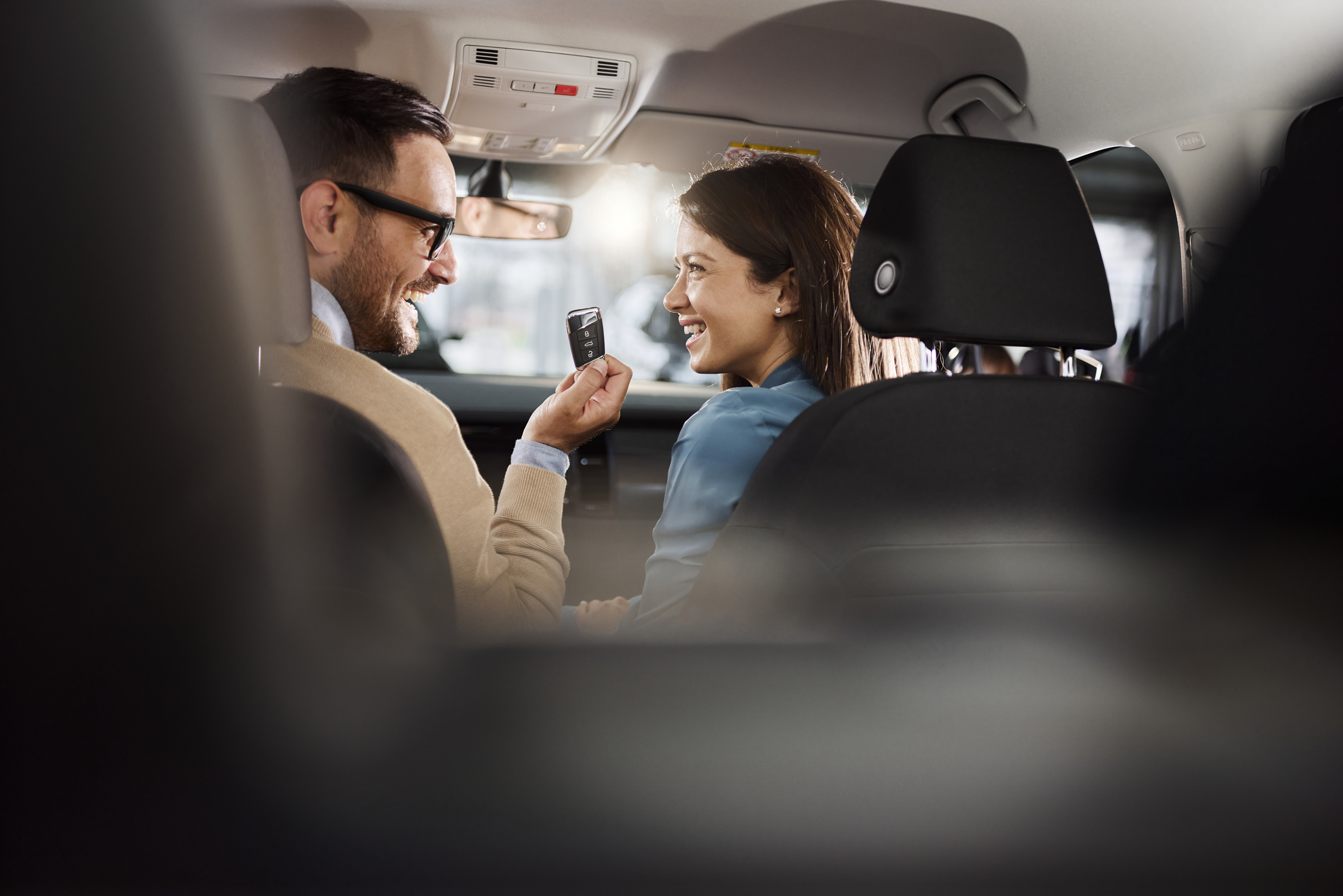Young happy couple talking about keys while sitting inside of their new car.