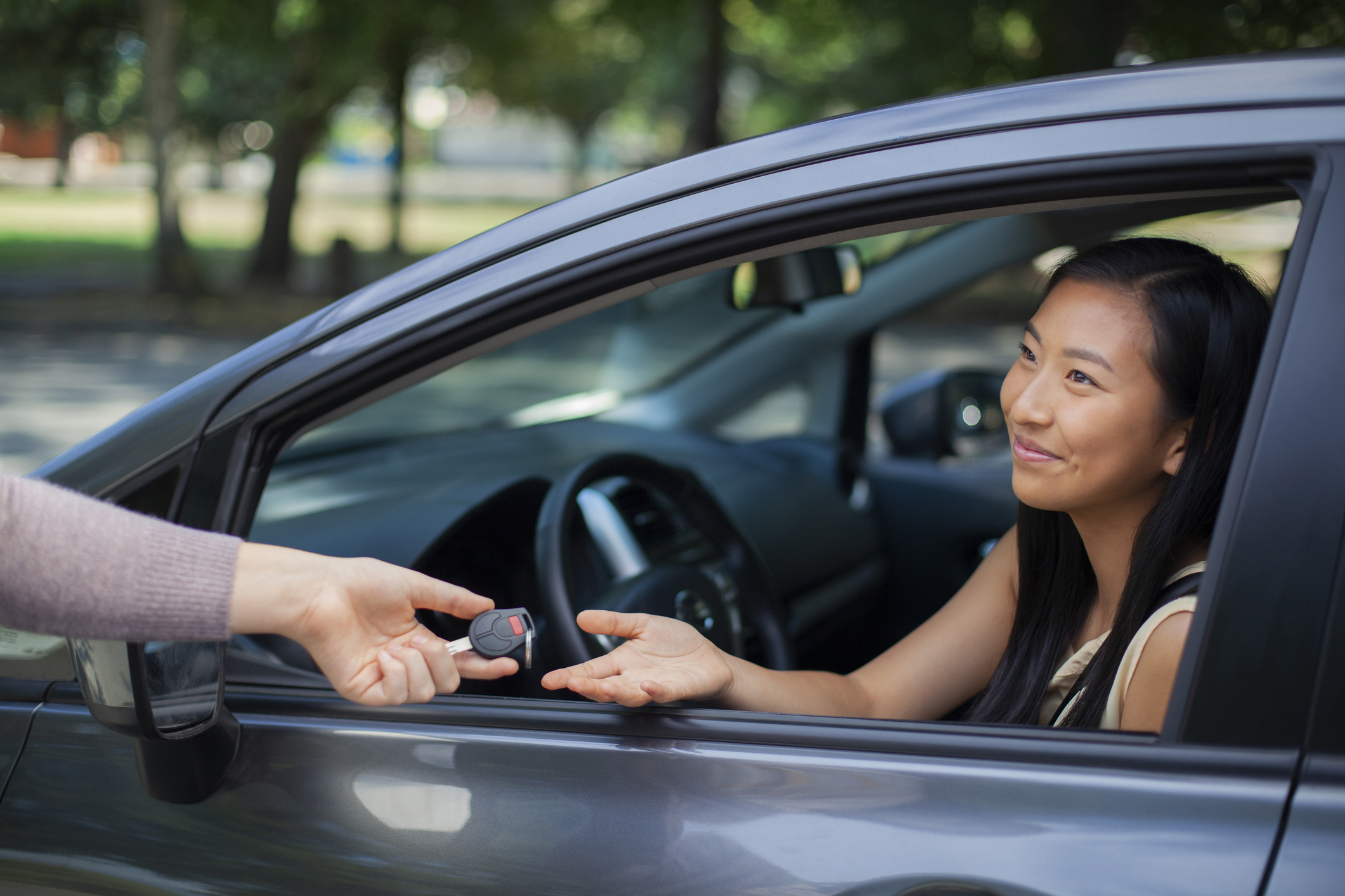 Young girl new driver receives car key from another person while sitting in the car.